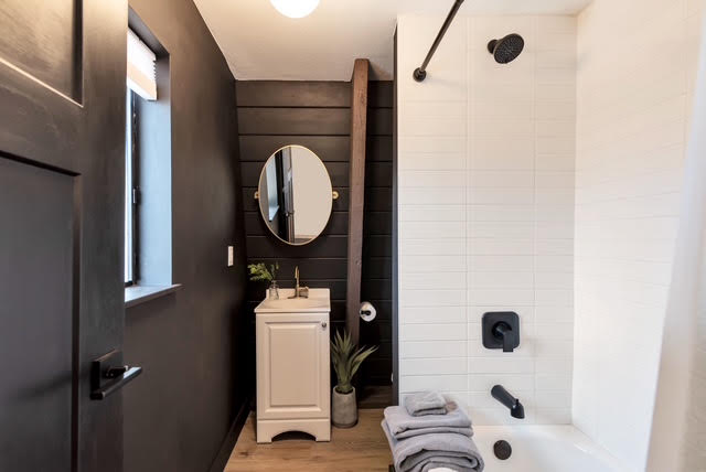 The renovated bathroom with a modern vanity, black accents, and a new shower surround