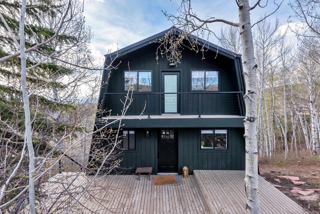 The cabin's exterior after a full renovation, dark modern siding and a new deck