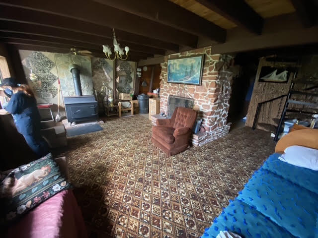 The cabin's original family room with a dated wood stove and worn carpet