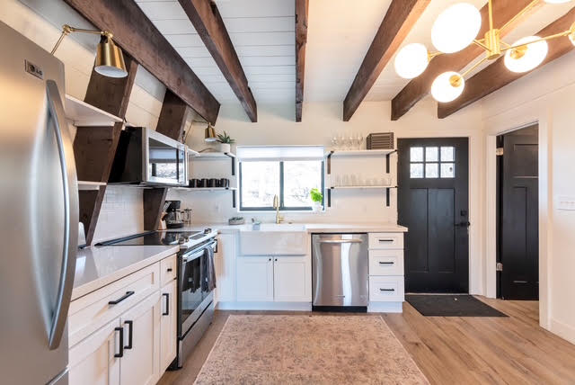The renovated kitchen with white cabinetry, open shelving, and exposed wood beams