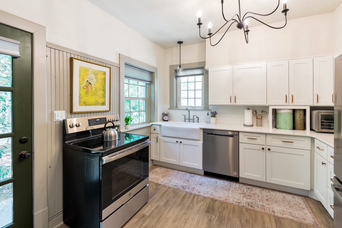 The renovated kitchen with white shaker cabinets, a farmhouse sink, and stainless appliances