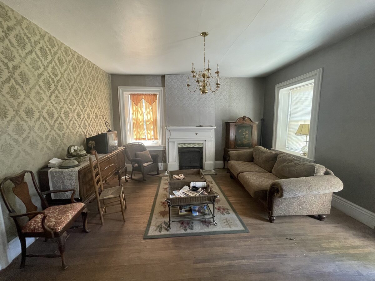 The home's original living room with dated wallpaper and worn furnishings